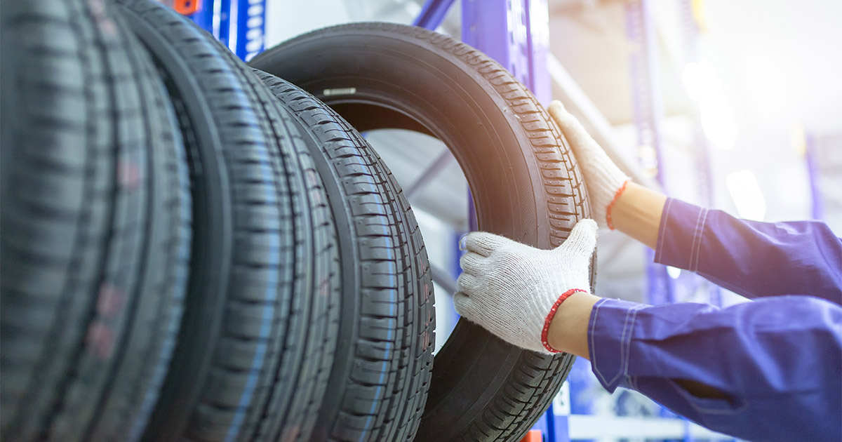 Mechanic wearing gloves inspects car tire in automotive workshop, checking tire tread and condition