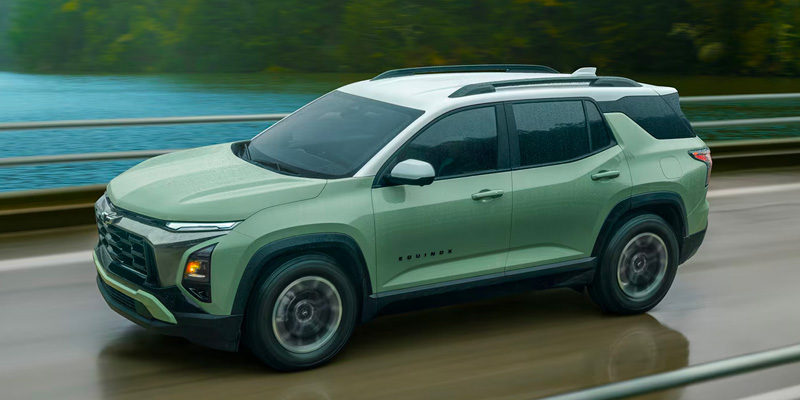 A 2026 Chevrolet Equinox SUV drives along a road beside a body of water, with blurred greenery in the background suggesting motion.
